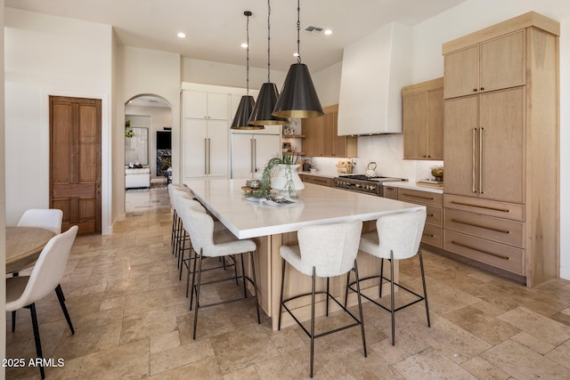 kitchen featuring arched walkways, high quality appliances, a breakfast bar, stone tile flooring, and a large island with sink