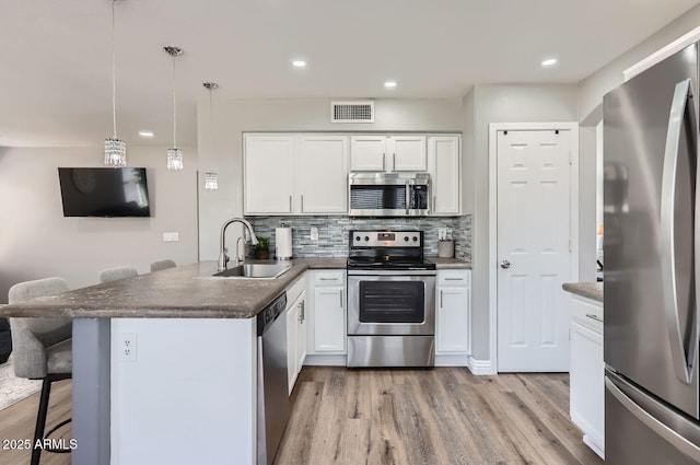 kitchen featuring stainless steel appliances, a breakfast bar, a sink, white cabinetry, and dark countertops