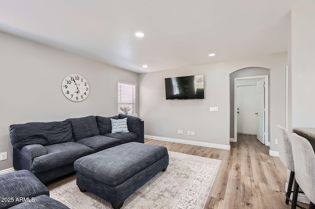 living room featuring arched walkways, recessed lighting, baseboards, and light wood-style floors