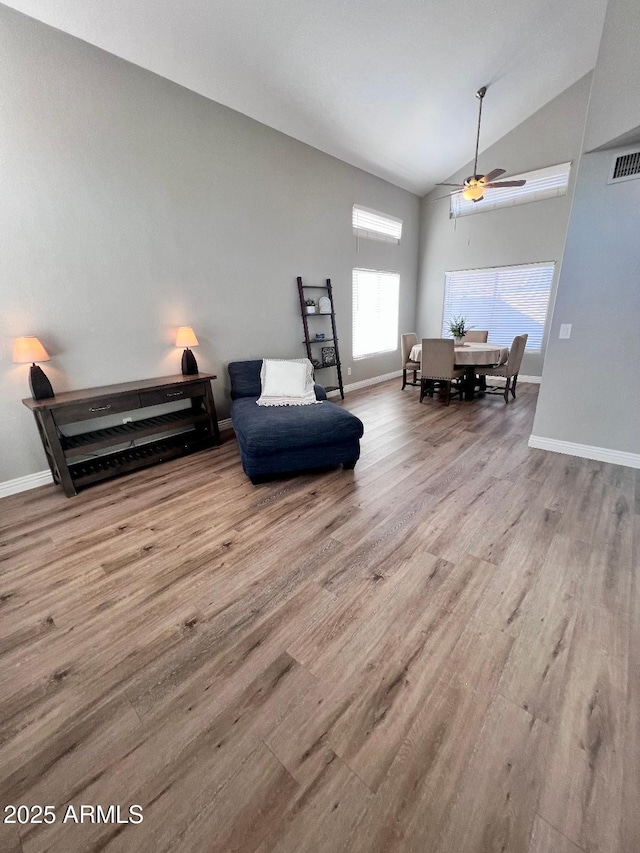 living area featuring high vaulted ceiling, light wood-style flooring, visible vents, and baseboards