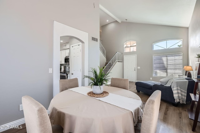 dining area with arched walkways, stairway, wood finished floors, high vaulted ceiling, and beamed ceiling