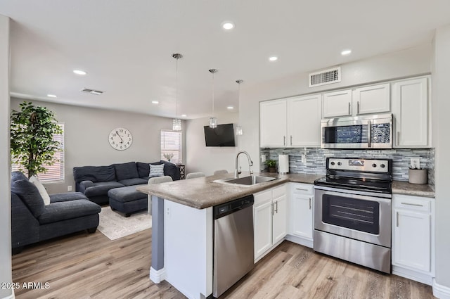 kitchen with visible vents, hanging light fixtures, appliances with stainless steel finishes, open floor plan, and a sink