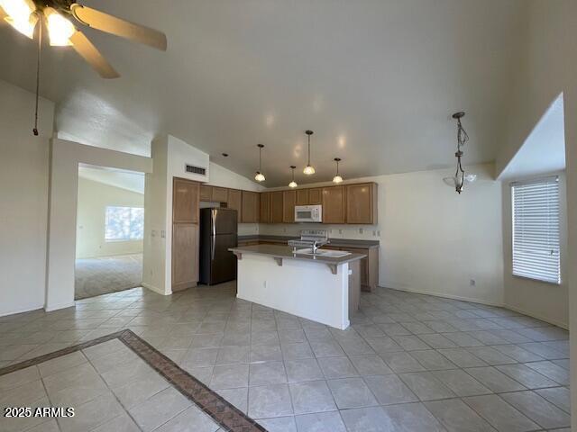 kitchen featuring black refrigerator, pendant lighting, lofted ceiling, a breakfast bar area, and a center island with sink