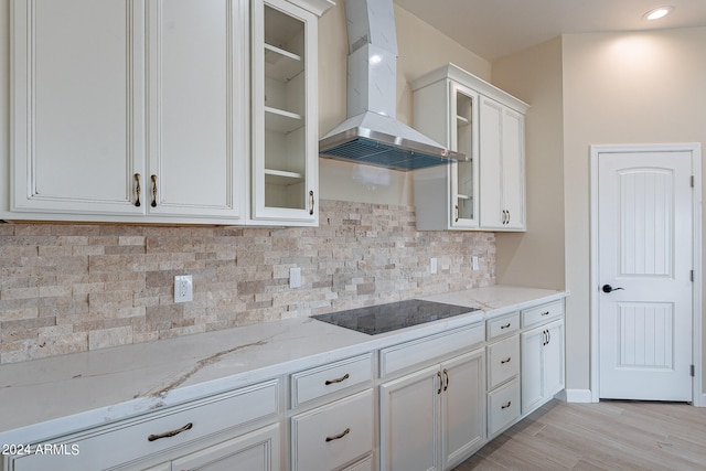 kitchen featuring decorative backsplash, black electric cooktop, wall chimney exhaust hood, light wood-type flooring, and white cabinets