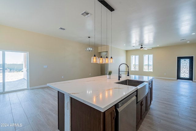 kitchen featuring sink, light wood-type flooring, hanging light fixtures, stainless steel dishwasher, and a kitchen island with sink