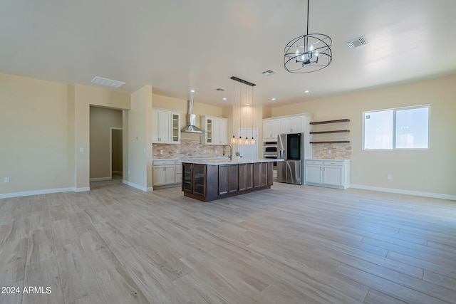 kitchen featuring stainless steel fridge, backsplash, a kitchen island with sink, light hardwood / wood-style floors, and decorative light fixtures