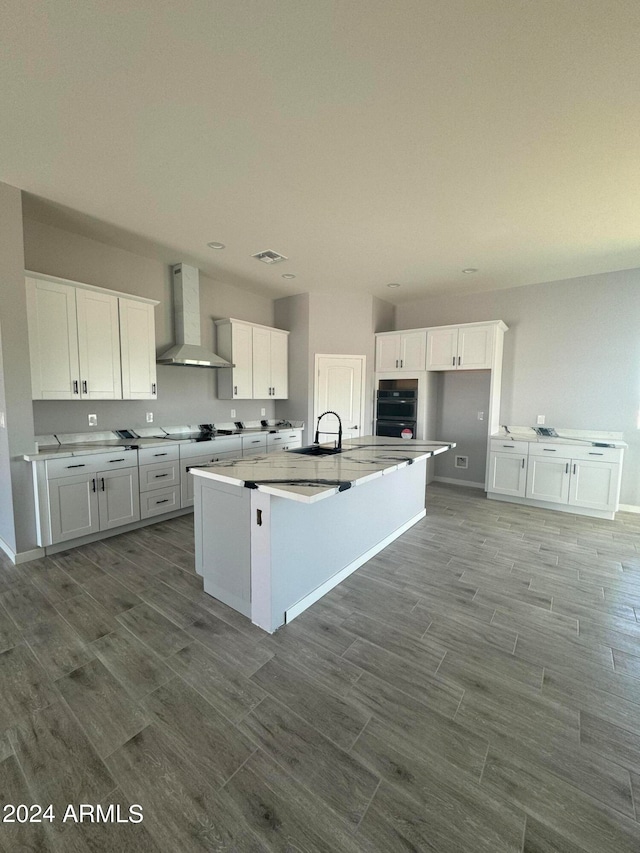 kitchen featuring sink, white cabinetry, wall chimney range hood, and an island with sink