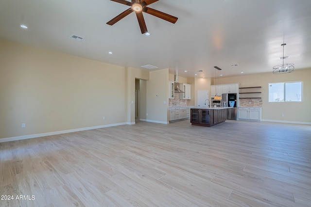 unfurnished living room with light hardwood / wood-style floors, sink, and ceiling fan with notable chandelier