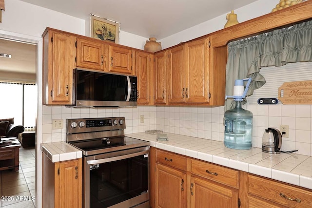 2619 W Lamar Rd, Phoenix, AZ 85017 - kitchen with tile patterned flooring, backsplash, light countertops, brown cabinets, and stainless steel electric range