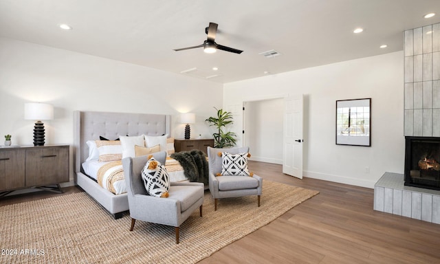 bedroom featuring ceiling fan, a tile fireplace, and hardwood / wood-style flooring