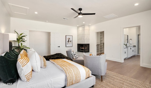 bedroom featuring ceiling fan, a tile fireplace, connected bathroom, light hardwood / wood-style floors, and a walk in closet