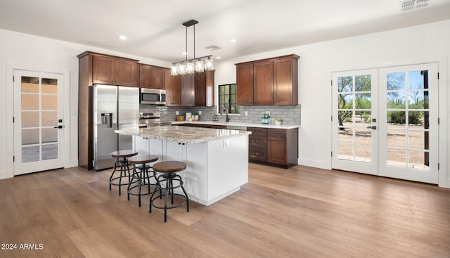 kitchen featuring pendant lighting, backsplash, appliances with stainless steel finishes, a kitchen island, and light hardwood / wood-style floors