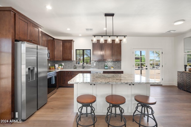 kitchen with appliances with stainless steel finishes, a center island, light wood-type flooring, and pendant lighting