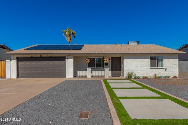 single story home featuring a garage, solar panels, and covered porch