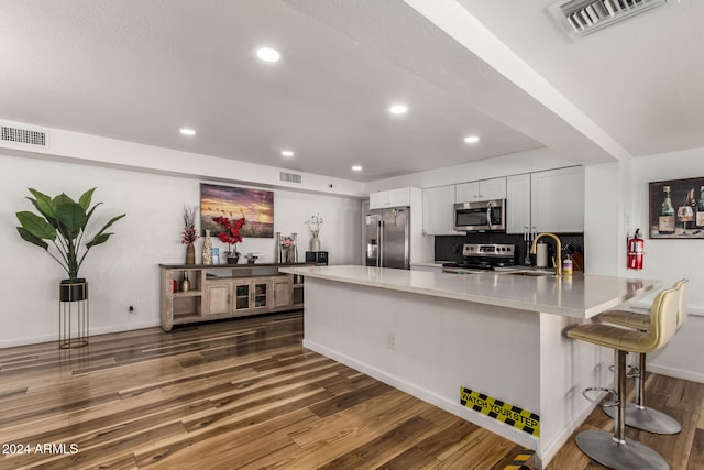 kitchen featuring sink, a breakfast bar, appliances with stainless steel finishes, white cabinets, and dark hardwood / wood-style flooring