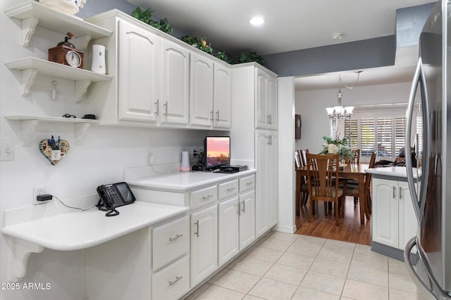 kitchen featuring stainless steel refrigerator, white cabinets, hanging light fixtures, light tile patterned floors, and a notable chandelier