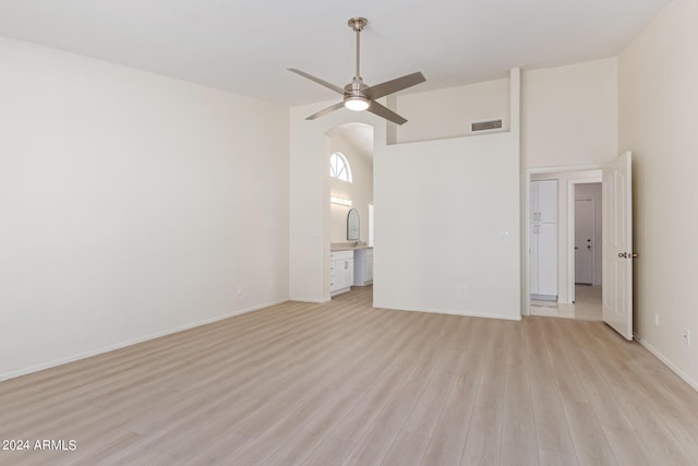 empty room with ceiling fan, a towering ceiling, and light hardwood / wood-style flooring