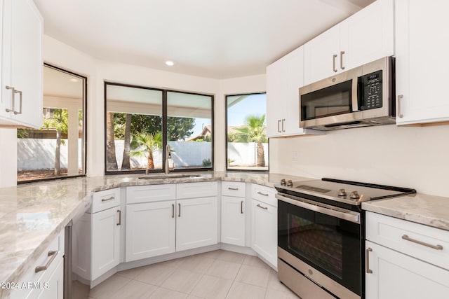 kitchen with sink, light stone countertops, light tile patterned floors, white cabinetry, and stainless steel appliances