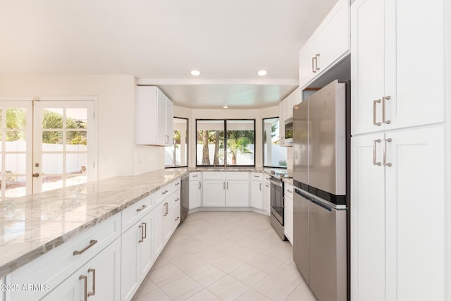 kitchen with a wealth of natural light, white cabinetry, light stone countertops, and appliances with stainless steel finishes