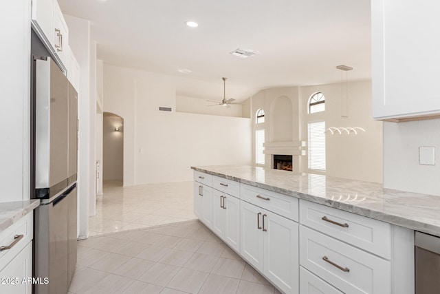 kitchen featuring white cabinets, ceiling fan, light stone countertops, and stainless steel refrigerator