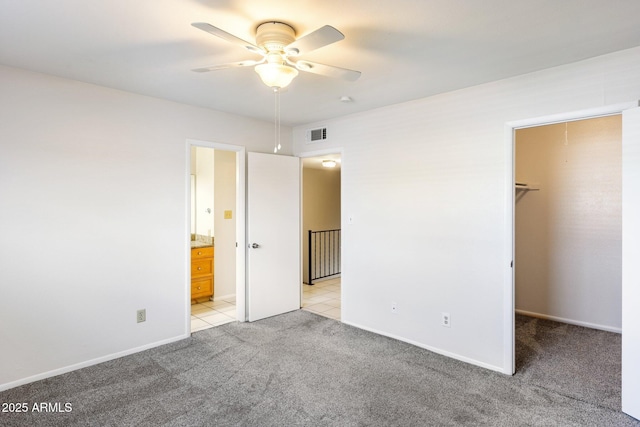 unfurnished bedroom with ensuite bath, a spacious closet, light carpet, a closet, and ceiling fan