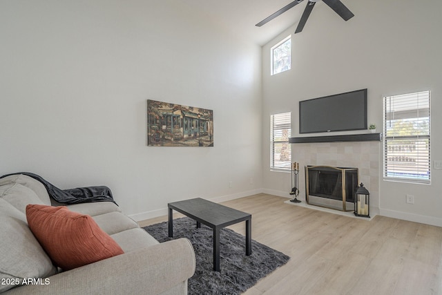 living room with ceiling fan, a fireplace, a high ceiling, and light wood-type flooring