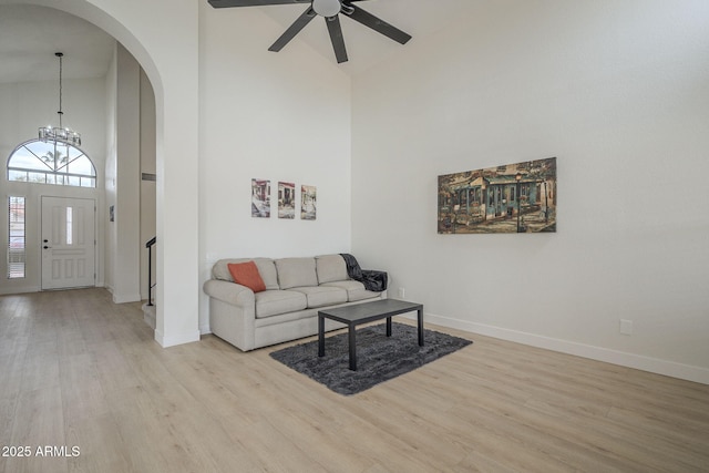 living room featuring high vaulted ceiling, ceiling fan with notable chandelier, and light hardwood / wood-style floors