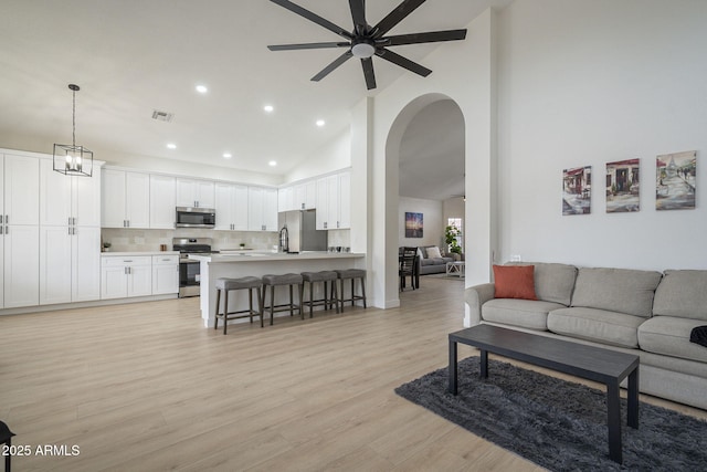 living room with ceiling fan with notable chandelier, light hardwood / wood-style floors, and high vaulted ceiling