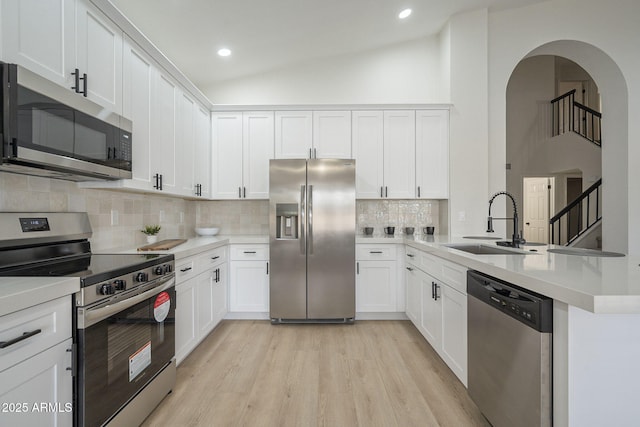 kitchen with lofted ceiling, sink, appliances with stainless steel finishes, light hardwood / wood-style floors, and white cabinets