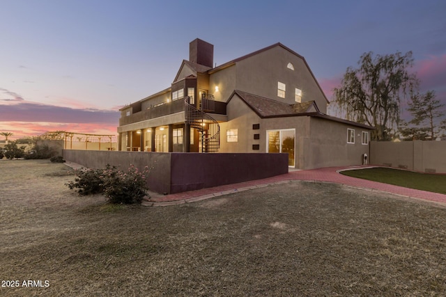 back house at dusk with a yard and a balcony