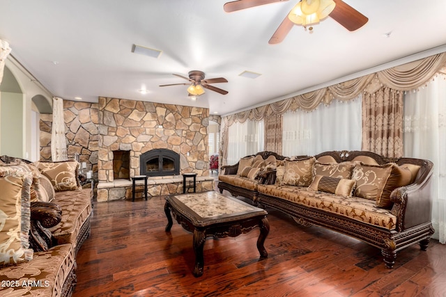 living room featuring dark hardwood / wood-style flooring, a healthy amount of sunlight, a stone fireplace, and ceiling fan