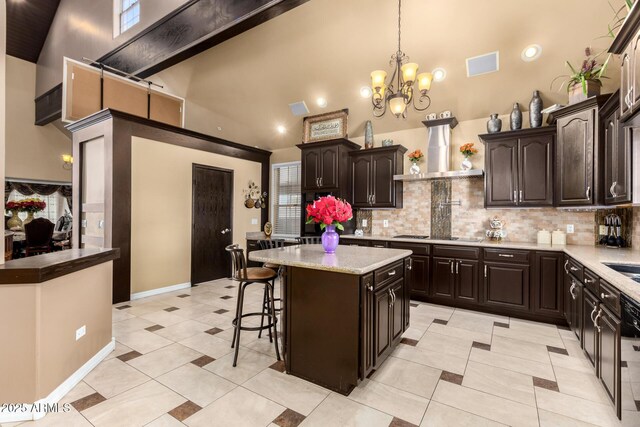 kitchen with tasteful backsplash, wall chimney exhaust hood, dark brown cabinetry, pendant lighting, and a kitchen island