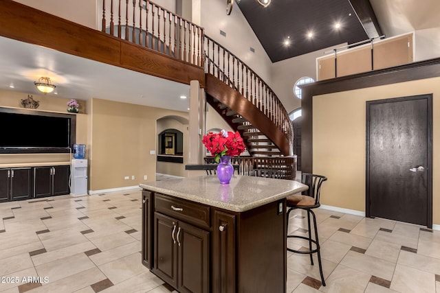 kitchen featuring dark brown cabinetry, light stone counters, a towering ceiling, a breakfast bar, and a kitchen island