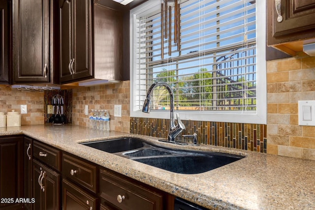 kitchen with light stone countertops, dark brown cabinetry, sink, and tasteful backsplash