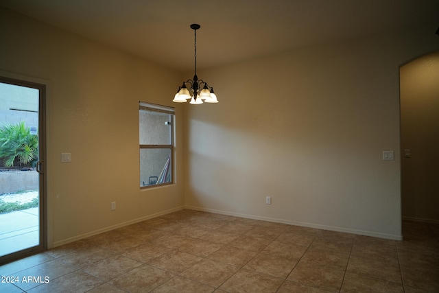 tiled spare room featuring an inviting chandelier