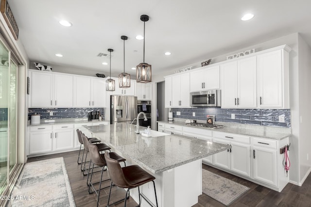 kitchen with sink, hanging light fixtures, stainless steel appliances, a center island with sink, and white cabinets