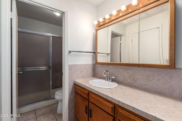 bathroom featuring vanity, a stall shower, tile patterned floors, toilet, and tile walls