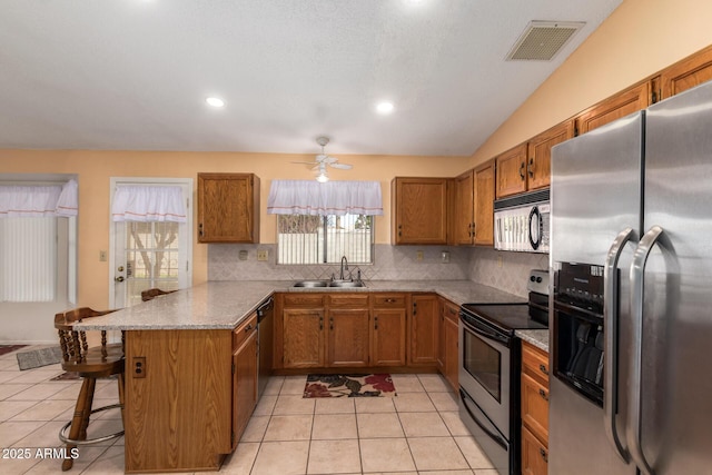 kitchen with visible vents, a peninsula, brown cabinetry, stainless steel appliances, and a sink