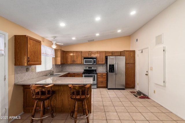 kitchen featuring brown cabinets, a sink, stainless steel appliances, a peninsula, and vaulted ceiling