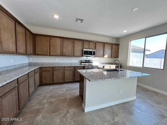 kitchen with light stone countertops, stainless steel appliances, sink, and a center island with sink