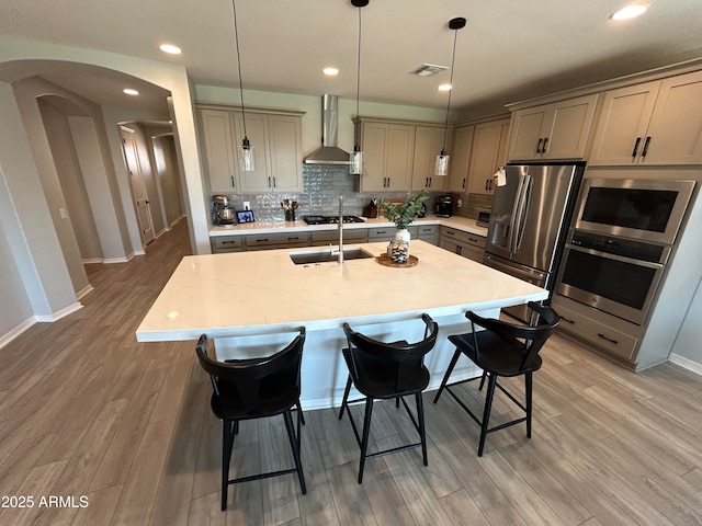 kitchen with stainless steel appliances, arched walkways, gray cabinets, and wall chimney range hood