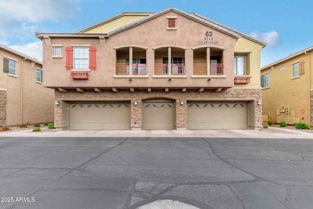 view of front of home with an attached garage, stucco siding, asphalt driveway, and a balcony