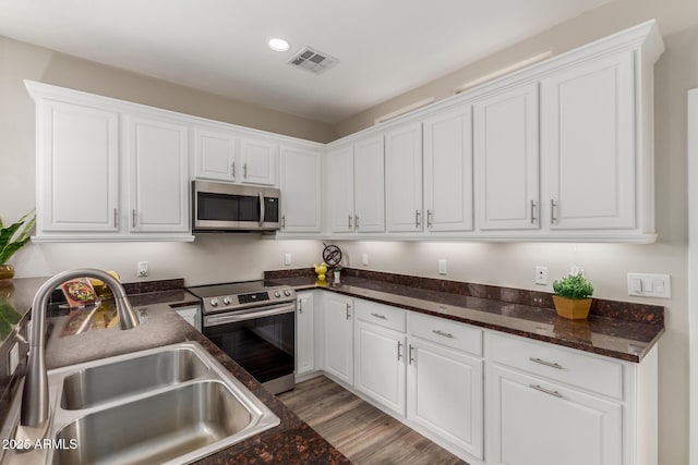 kitchen with appliances with stainless steel finishes, a sink, white cabinets, recessed lighting, and light wood-style floors