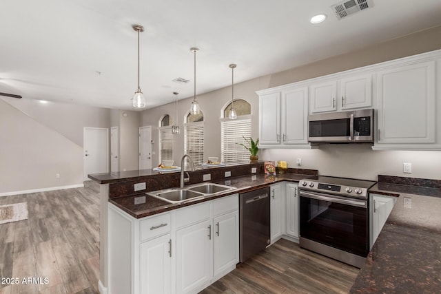 kitchen featuring appliances with stainless steel finishes, a sink, a peninsula, wood finished floors, and white cabinetry