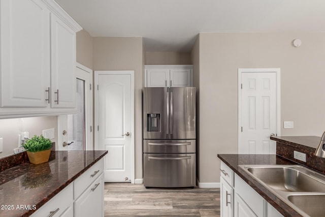 kitchen featuring stainless steel fridge, a sink, light wood-style floors, white cabinets, and baseboards