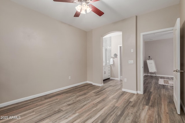 unfurnished room featuring a ceiling fan, wood finished floors, arched walkways, and baseboards