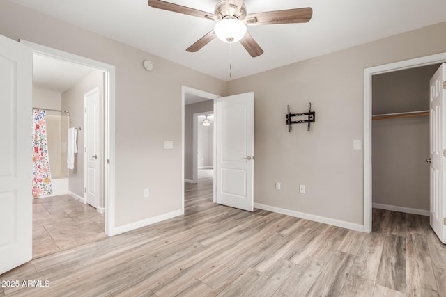 unfurnished bedroom with light wood finished floors, a closet, baseboards, and a spacious closet