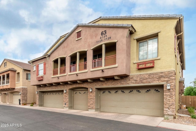 view of front of home featuring stone siding, an attached garage, stucco siding, and driveway