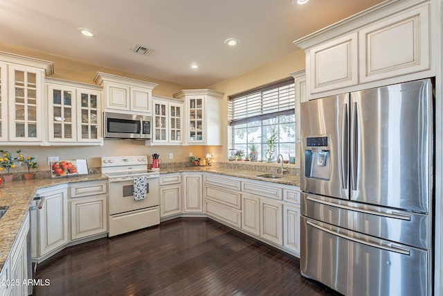 kitchen with appliances with stainless steel finishes, dark hardwood / wood-style floors, cream cabinets, sink, and light stone countertops