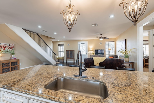 kitchen featuring stone countertops, ceiling fan with notable chandelier, sink, and pendant lighting